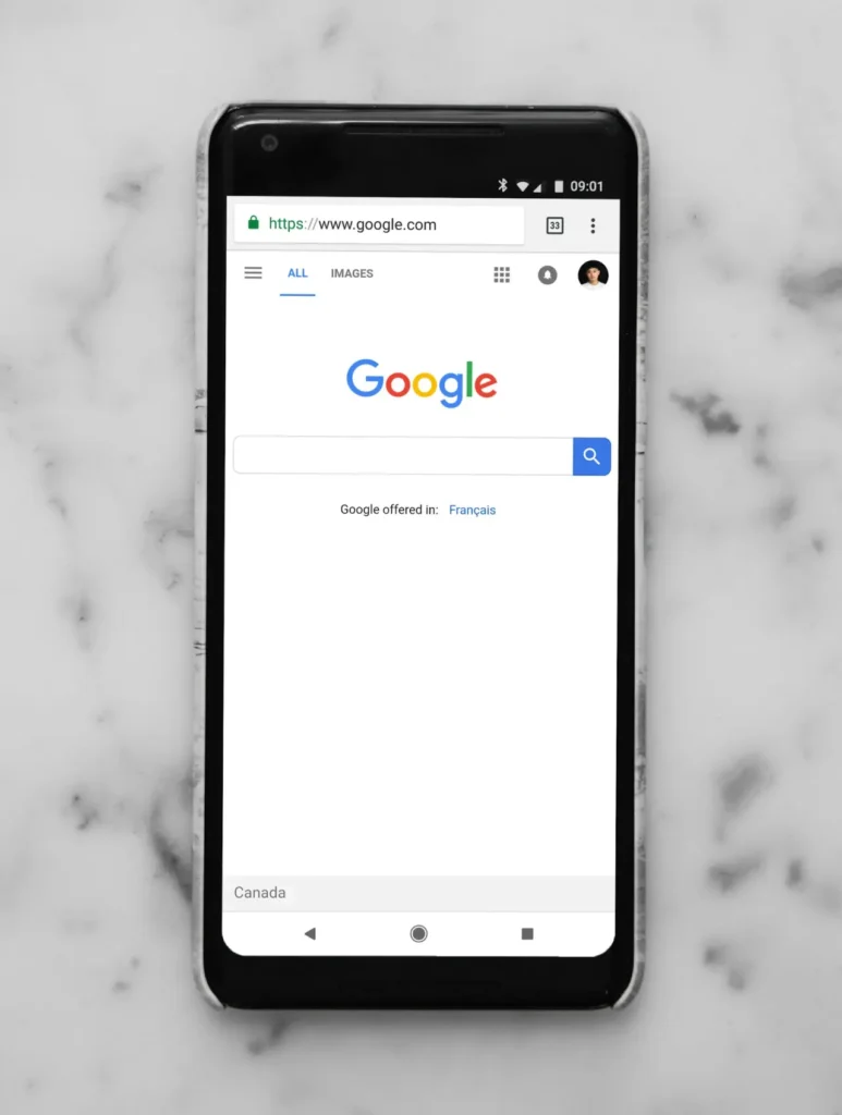 A smartphone showcasing the Google homepage with its search bar and language options rests on a white marble surface, much like the foundation for effective HARO link building.