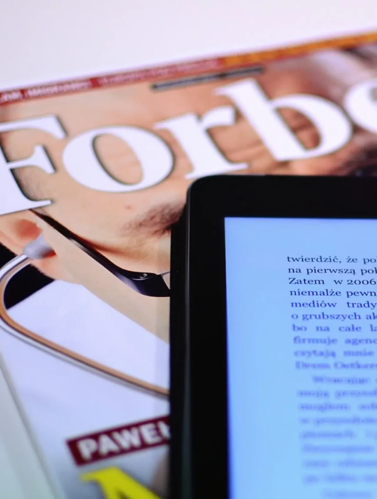 A tablet displaying text rests atop a Forbes magazine. The cover, featuring a close-up of someone with a stethoscope, hints at a medical or professional theme, seamlessly blending traditional media influence with modern strategies like HARO link building in the digital realm.