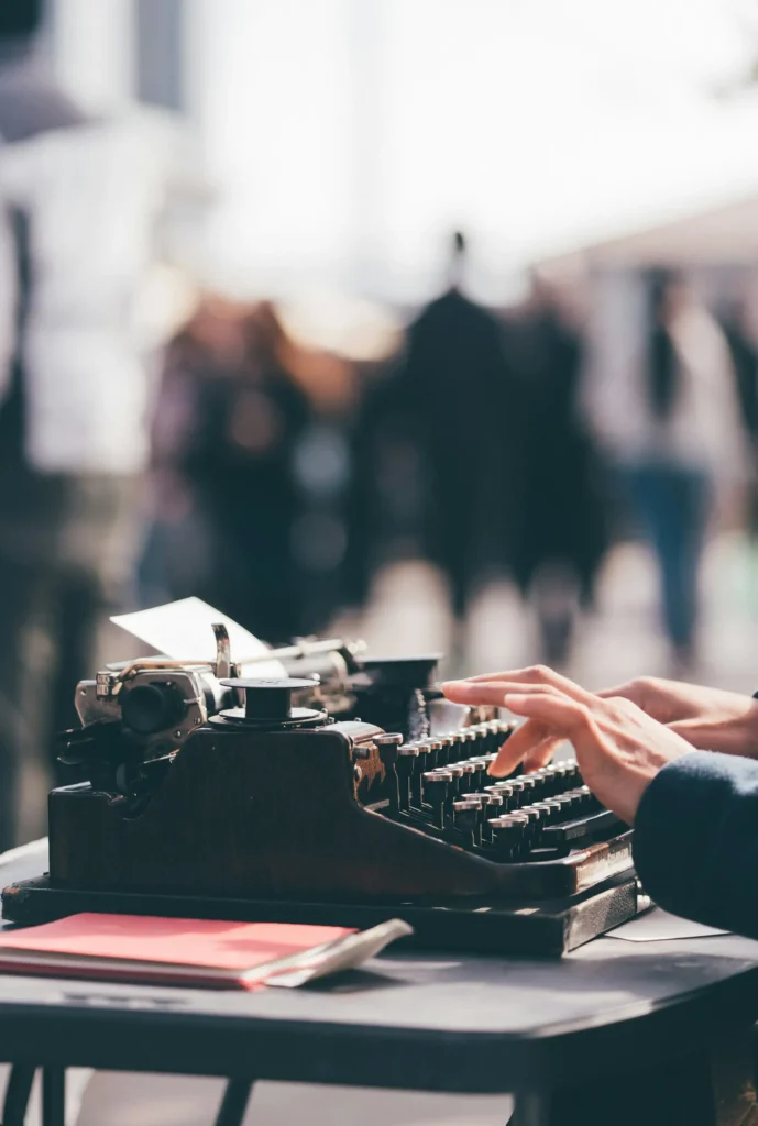 Close-up of a person expertly typing on a vintage typewriter, outdoors. The background is blurred, showing people engaged in haro link building while basking in the soft natural light.