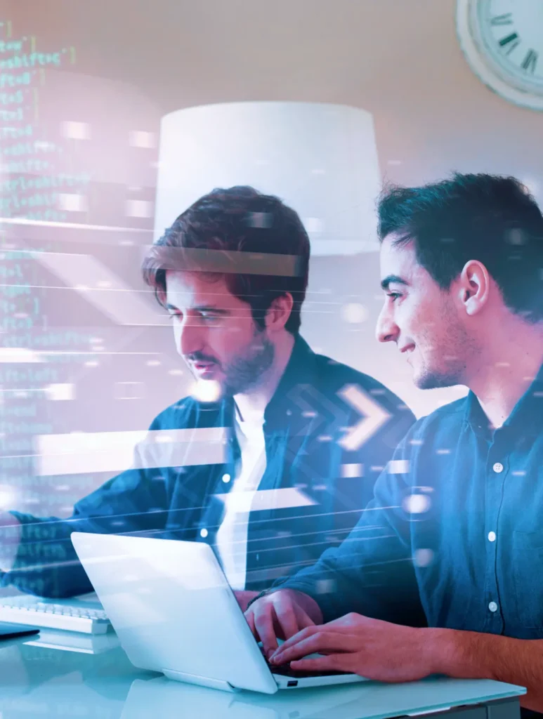 Two men working on laptops in an office setting with holographic digital code and graphics overlaying the scene, indicating a focus on technology or programming. A clock is visible in the background.