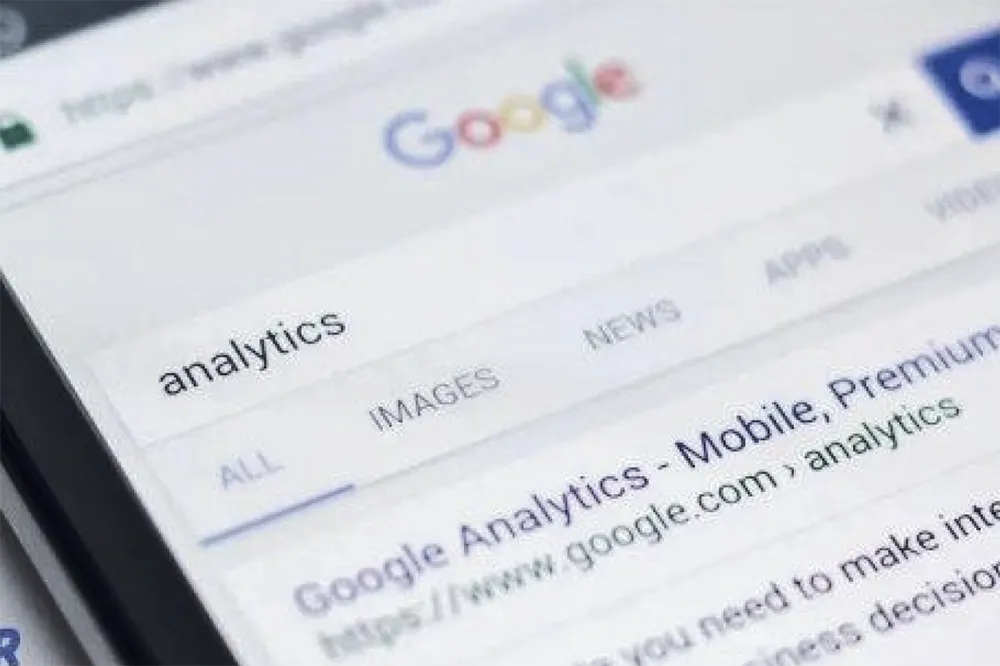 A smartphone screen displays a Google search results page for the term "analytics," showing options like "All," "Images," "News," and "Apps." Below is a link to "Google Analytics - Mobile, Premium" from a website.