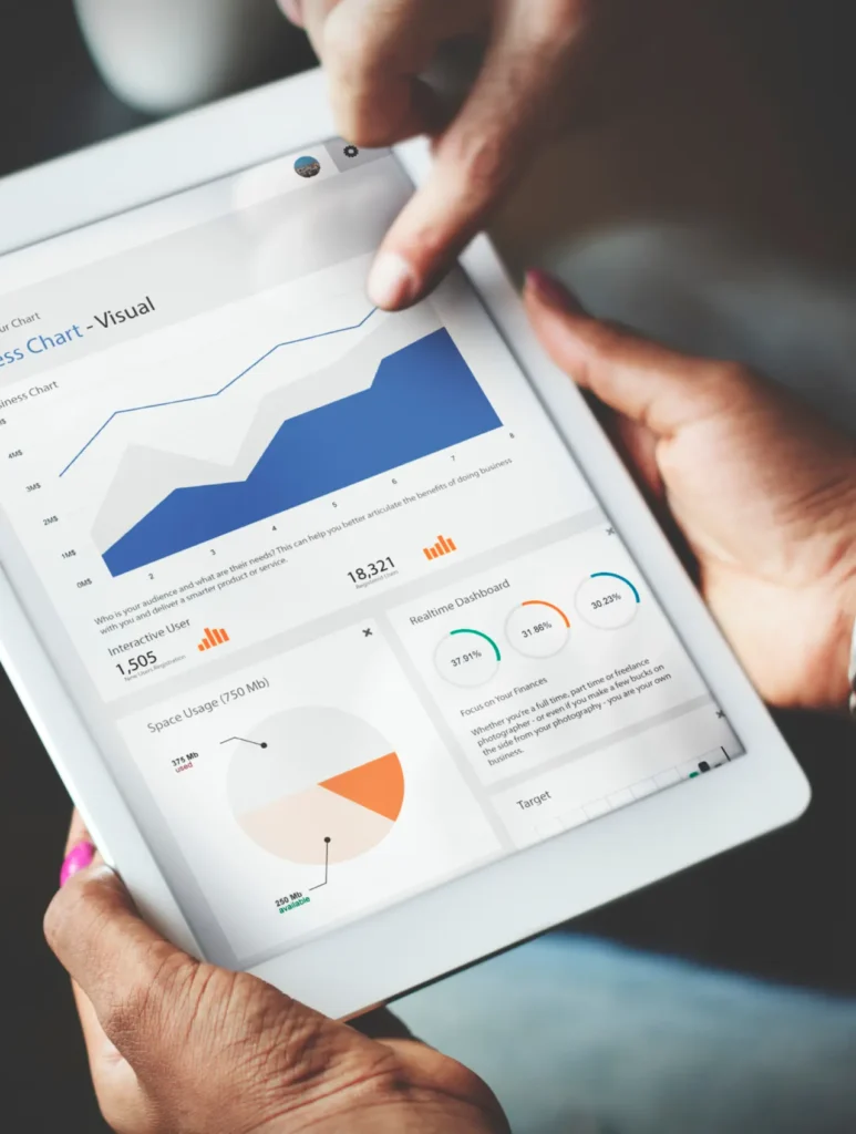Person holding a tablet displaying various data visualizations, including a line chart, bar graphs, and pie chart. The charts show numerical data and performance metrics.