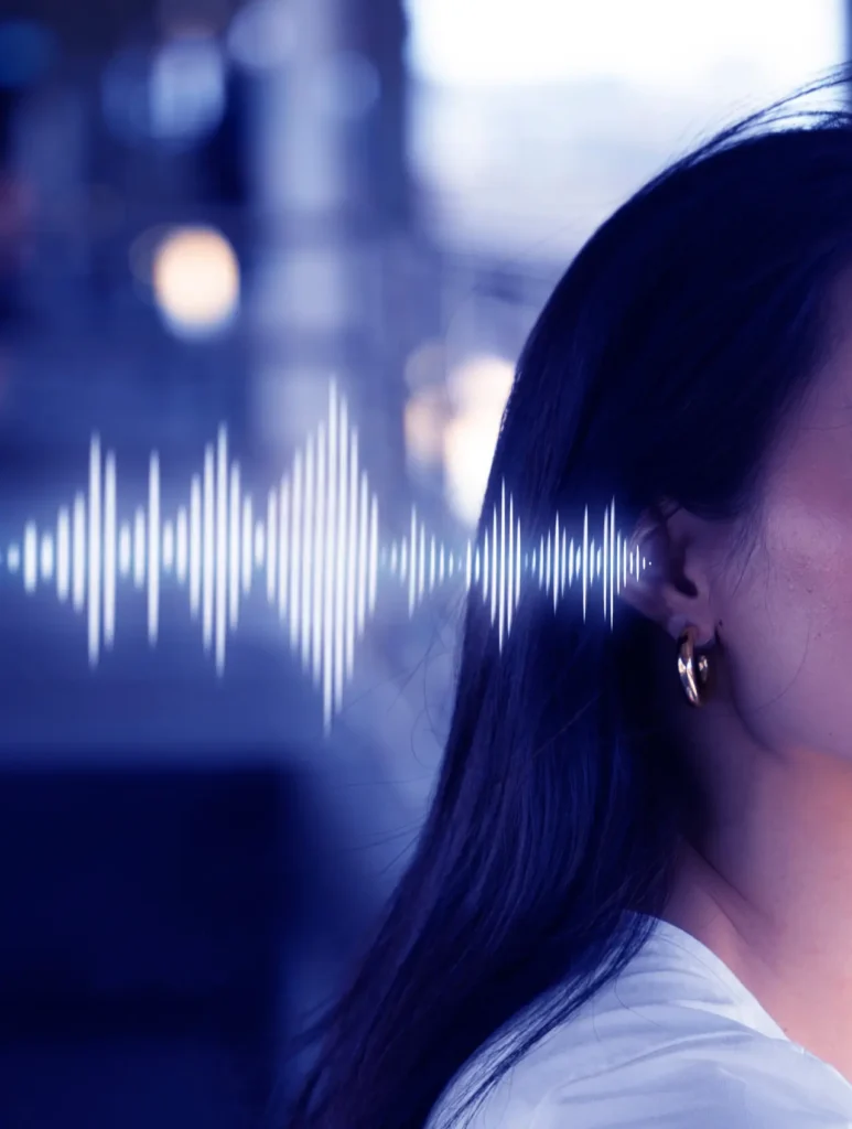A woman's side profile with long dark hair and gold hoop earrings, set against a blurred background. A digital sound wave graphic is superimposed near her ear, suggesting audio or communication technology.